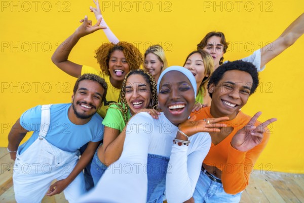 Frontal view of a multi-ethnic group of friends gesturing happily while taking a selfie in a yellow