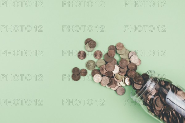 above view of small change Euro coins spilling out of glass jar on green background