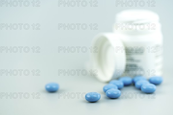 horizontal selective focus close up of white prescription pill bottle and blue pills