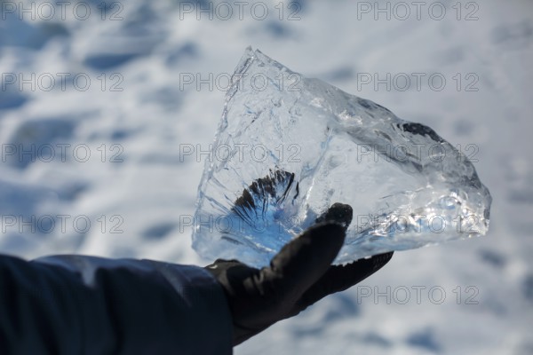 Happy smiling man wearing winter blue jacket and holding piece of transparent crushed ice cubes in