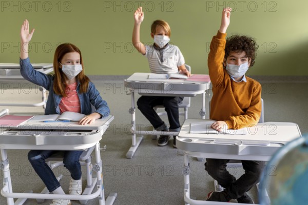 Front view children with medical masks school raising their hands