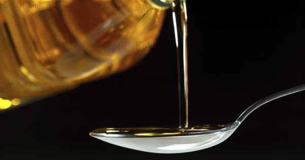 Olive Oil Pouring from Spoon on Black Background