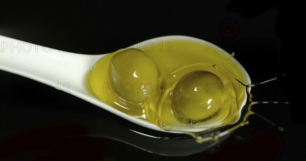 Green Olive, Olea europaea, Falling in a Spoon against Black Background