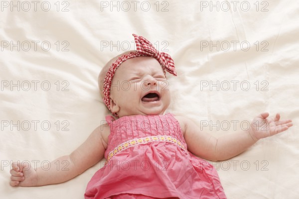 Crying and gesturing ten weeks old baby girl on bed