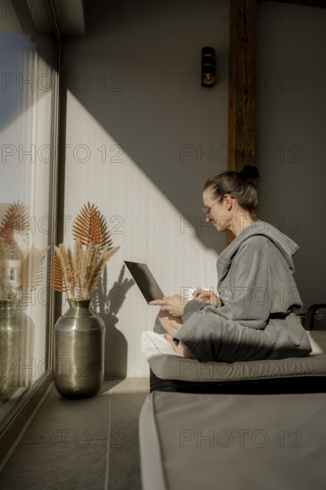 Woman in bathrobe sitting with a laptop on her lap in a garden