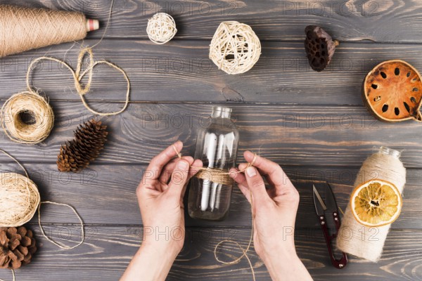 Female hand tying glass bottle with string near cutter dry lotus pod dried fruit slices pine cone