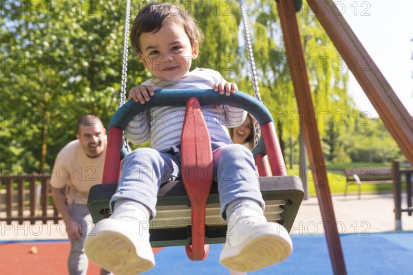 Frontal view of parents swinging a small child at the playground in a sunny day