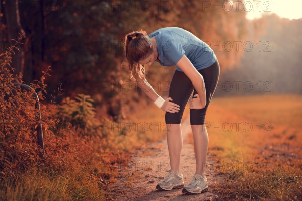 Young athletic woman taking a break from training standing resting her hands on her knees on a