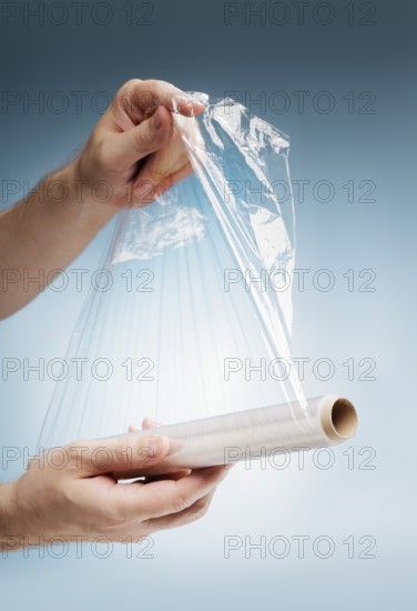 Man holding a roll of plastic film, typically used for sealing food items