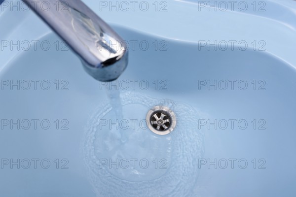 Water flows from the tap in a blue washbasin. The liquid pours out, swirling, in the open plug