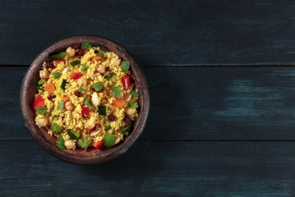 Vegan couscous with vegetables, almonds, chickpeas and herbs, shot from above on a dark wooden