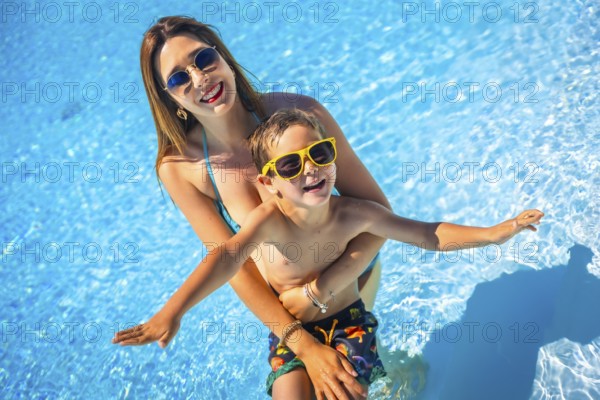 Happy family of a caucasian mother and boy having fun together inside a swimming pool in summer