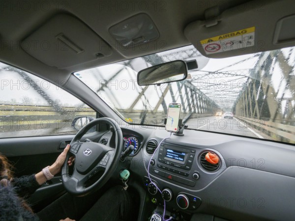View from inside a car on a rainy day driving over a bridge with a phone for navigation, A1 A8