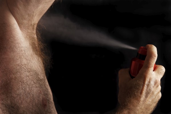 Man with chest hair spraying deodorant into his armpit