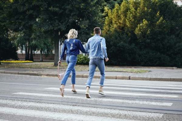 Back view of young happy couple running crosswalk in the street. Fun, walking, dating concept