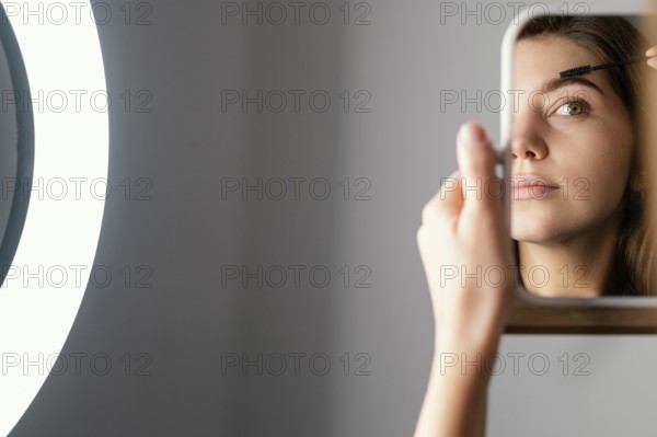 Woman brushing her eyebrows while looking mirror after treatment with copy space