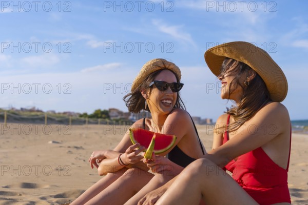 Portrait of female friends on summer beach vacation eating a watermelon with the sea in the