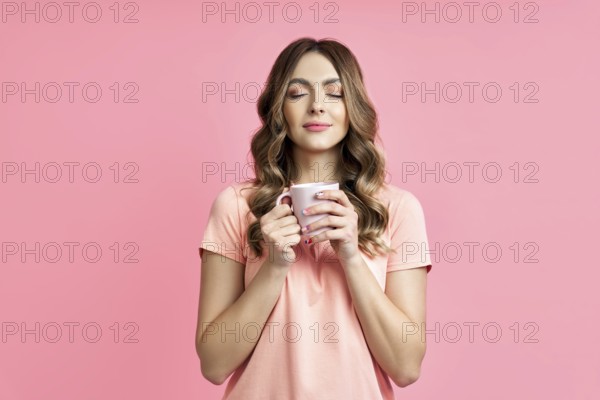 Young pretty woman enjoying cup of aroma coffee closed eyes on pink background. Relax and rest