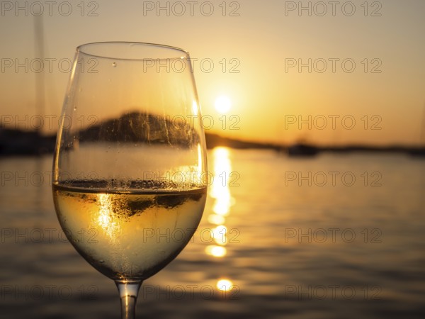 Sunset shimmering through a glass of white wine, evening mood in the harbour, boats and sailing