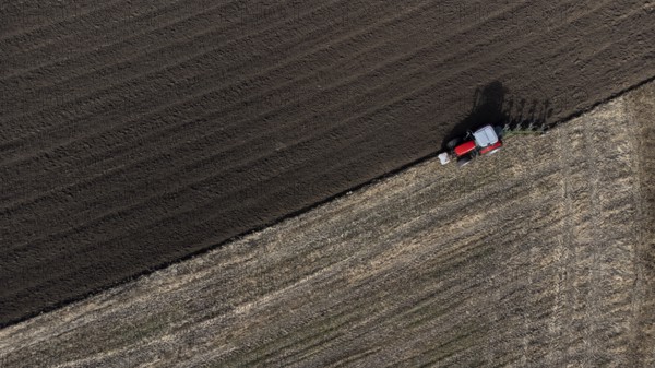 A red tractor ploughs a harvested field, dark soil, bird's eye view, drone shot, Upper Bavaria,