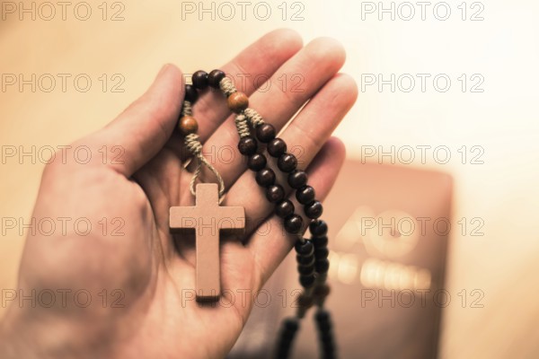 Man is holding a rosary, bible in the background