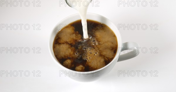 Milk poured into a Cup of Coffee against White Background