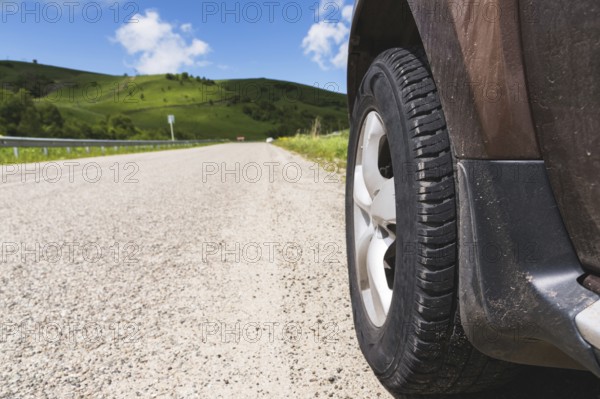 Close-up of a SUV wheel on an asphalt road outside the city against the green hills of blue sky and