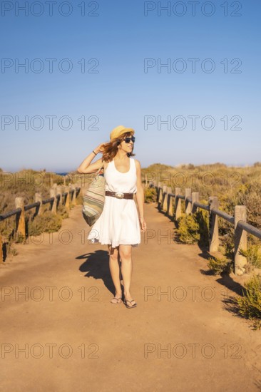 Vertical photo of a woman walking with a beach bag along a marked trail in Cabo de Gata, Spain,