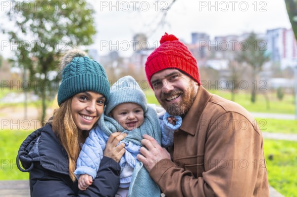 Smiling parents holding their baby, wearing winter clothes and wool hats, having fun together in a