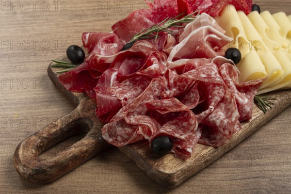 Assorted meat, appetizer, prosciutto, salami and ham, with maasdam cheese and olives, on a wooden