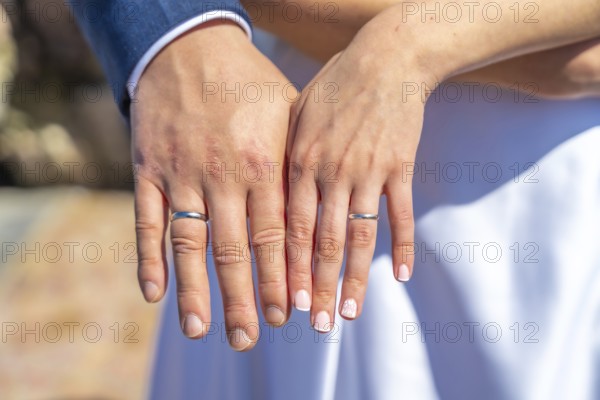 A couple is holding hands and wearing wedding rings. The man's ring is on the left hand and the
