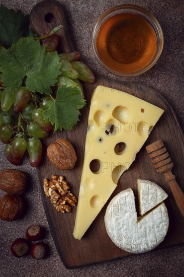 Cheese with big holes, emmental, maasdam, brie cheese, on a cutting board, with grapes and honey,
