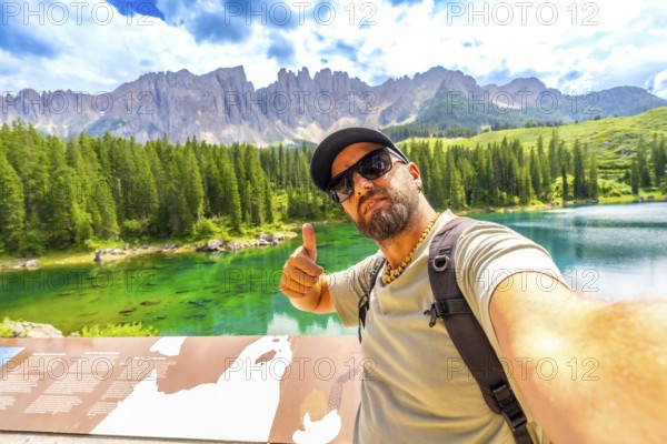 Tourist enjoying the breathtaking view of lake carezza and the dolomites making selfie and thumbs