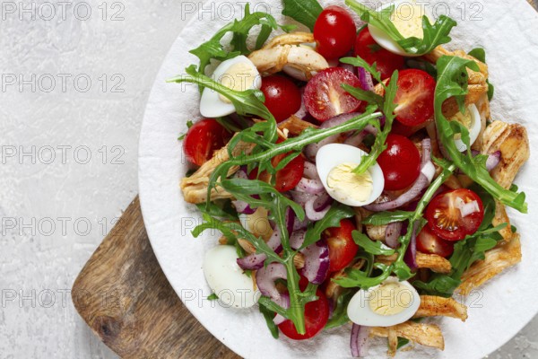 A warm salad with fried chicken fillet, arugula and cherry tomatoes, and boiled quail eggs, on a