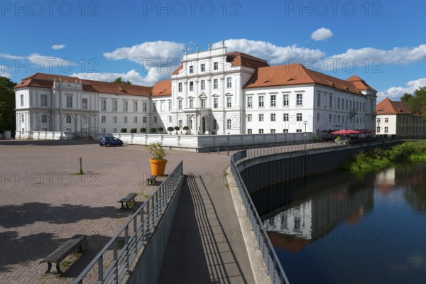 A baroque castle next to a bridge over a river, surrounded by flowering plants, Oranienburg Castle,