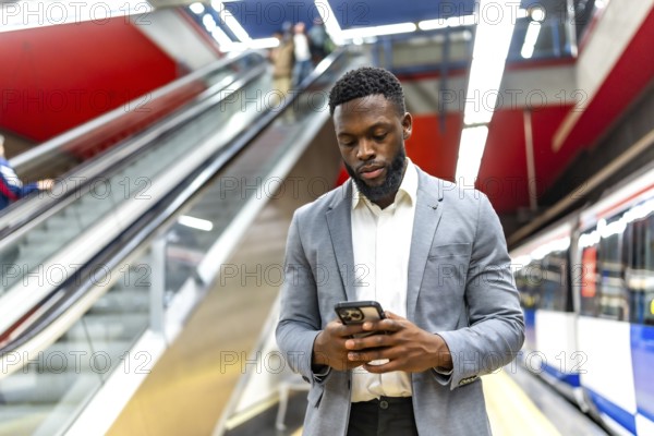 Young businessman waiting for a subway train in a station, using his smartphone to check messages