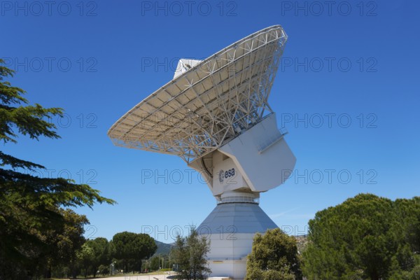ESA's large radio telescope under a clear blue sky, surrounded by green trees, for scientific use,