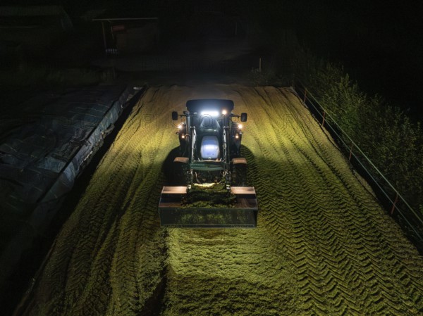 Tractor at night working on a silo filled with crop, maize harvest, Dachtel, Black Forest, Germany,