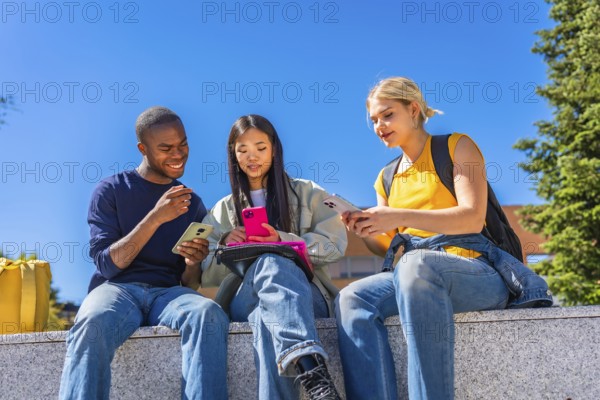Low angle view photo of a multiracial group of students using smartphones sitting outside the