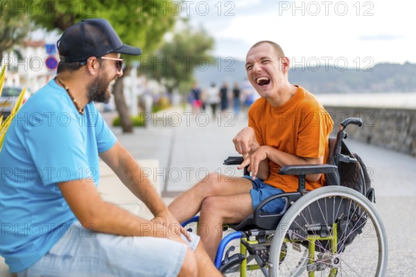 A disabled person in a wheelchair with a friend on summer vacation having fun laughing a lot by the