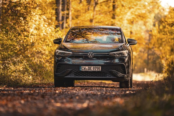 Car on forest road in autumn with colourful leaves and yellow light, electric car VW ID5,