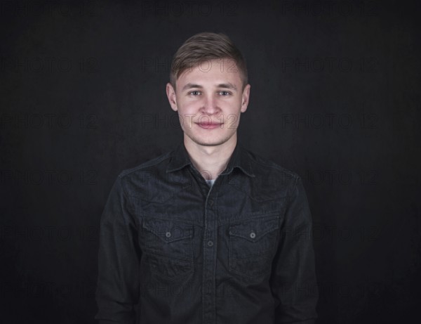 Portrait of a carefree young man against a black wall background looking to camera. Relaxed male