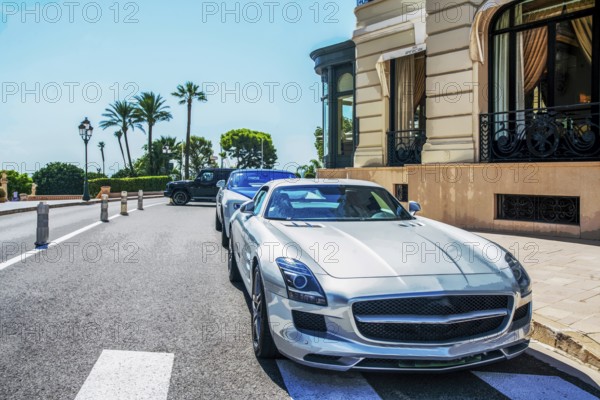 Luxury cars at parking lot in 5 meters from old building of casino Monte Carlo, behind palm trees