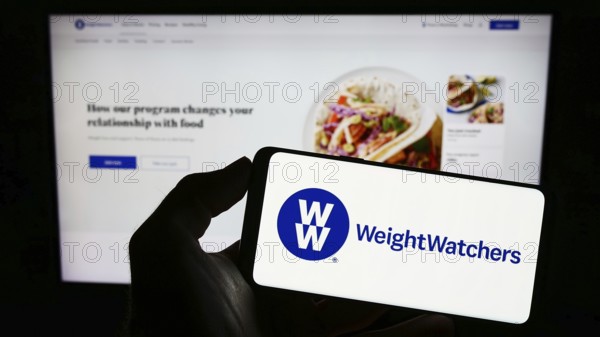 Stuttgart, Germany, 03-19-2023: Person holding cellphone with logo of WW International Inc. (Weight