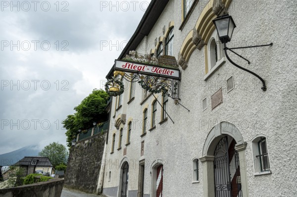 A traditional pub sign on a white wall of a European building on a cloudy day, Salzburg, Austria,