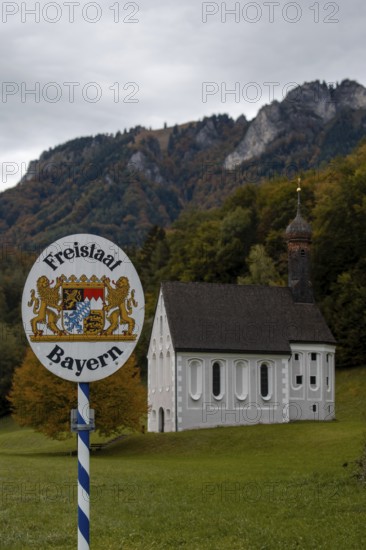 Free State of Bavaria sign with Nussdorf-Windshausen Kreuzkirche in the background, autumnal