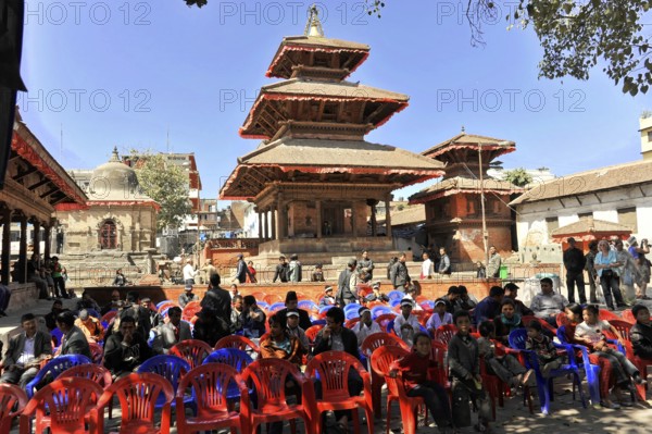 Group of people sitting on plastic chairs in front of a traditional temple, Kathmandu Valley,