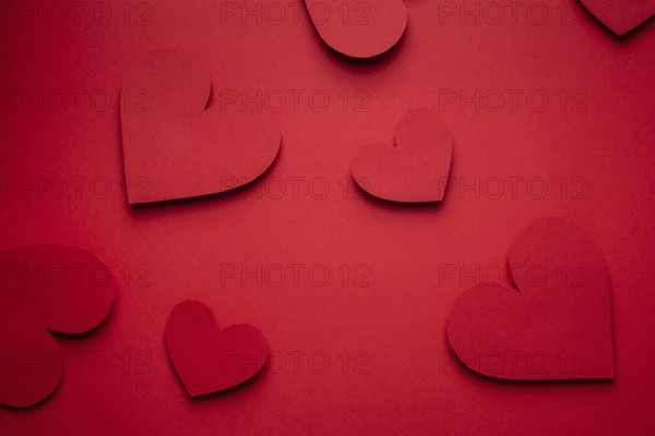 Red hearts cut from paper on red background, paper craft origami style, from above. Romantic