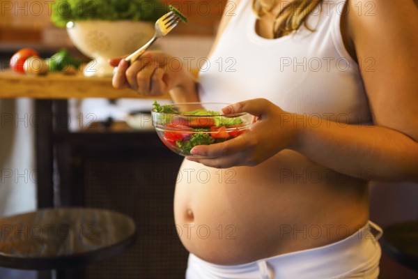 Young pregnant woman eating fresh vegetable salad at the kitchen. Pregnant nutrition