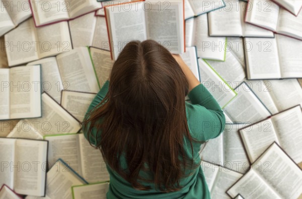 Top view of anonymous female student lying on books and reading during exam preparation